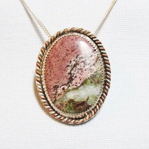 May include: A silver and copper pendant necklace with a pink, green, and white oval stone.