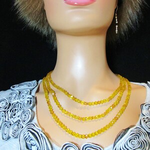 Puede incluir: Un collar de tres hilos con peque&ntilde;as cuentas amarillas facetadas. El collar est&aacute; en capas y descansa sobre el cuello de un maniqu&iacute;. Tambi&eacute;n se ven un par de pendientes colgantes con peque&ntilde;as cuentas.