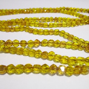 Puede incluir: Primer plano de varios hilos de cuentas amarillas facetadas. Las cuentas est&aacute;n ensartadas, creando un collar o elemento decorativo. Las cuentas tienen una superficie brillante y reflectante, y el color es un amarillo dorado c&aacute;lido.
