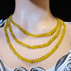 Puede incluir: Collar de tres hilos con cuentas de cristal amarillo facetadas. Las cuentas son peque&ntilde;as y de tama&ntilde;o uniforme, creando un efecto brillante. El collar se exhibe en un maniqu&iacute;, mostrando su dise&ntilde;o y ca&iacute;da.