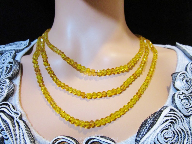 Puede incluir: Collar de tres hilos con cuentas de cristal amarillo facetadas. Las cuentas son peque&ntilde;as y de tama&ntilde;o uniforme, creando un efecto brillante. El collar se exhibe en un maniqu&iacute;, mostrando su dise&ntilde;o y ca&iacute;da.