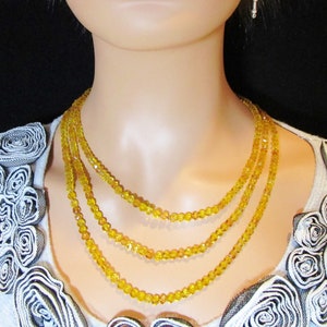 Puede incluir: Un collar de tres hilos con peque&ntilde;as cuentas amarillas facetadas. El collar es en capas y se usa en un maniqu&iacute;. El maniqu&iacute; lleva una camiseta gris claro con rosetas decorativas.