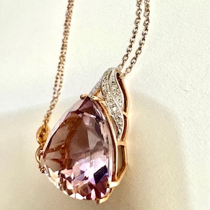 May include: A rose gold necklace featuring a large, faceted, light purple gemstone pendant. The pendant is pear-shaped and framed with a gold setting and a decorative accent of small, sparkling stones. The chain is delicate and also rose gold.