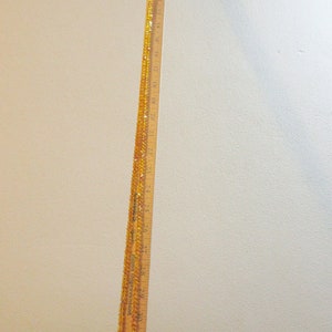 Puede incluir: Una regla de madera, de aproximadamente 91 cm de largo, con marcas en pulgadas y n&uacute;meros. Un hilo de cuentas de color &aacute;mbar est&aacute; drapeado a lo largo de la regla. La regla est&aacute; en &aacute;ngulo contra una superficie blanca y una pared beige.