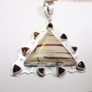 May include: A silver pendant featuring a triangular shaped stone with red and white stripes. The pendant is surrounded by a silver frame with eight small red stones.