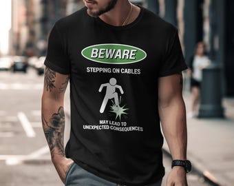 May include: Black t-shirt with a green and white warning sign that says "Beware Stepping on Cables May Lead to Unexpected Consequences". The sign features a stick figure stepping on a cable with a spark coming out.