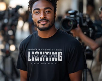 May include: A black t-shirt with white text that reads "KEEP GLOWING" and "STAY ILLUMINATED" above the word "LIGHTING" in large, bold letters. The text "PRECISION MASTER" is printed below the word "LIGHTING".