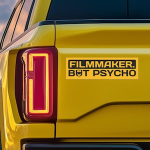 May include: A yellow truck with a black and yellow bumper sticker that reads "Filmmaker. But Psycho."