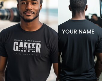 May include: Black crew neck t-shirt with the text "GAFFER STAY BRIGHT PRECISION MASTER" in white. The front of the shirt has the text "KEEP TAPING" above the word "GAFFER". The back of the shirt has the text "YOUR NAME" in white.