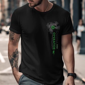 Pode incluir: T-shirt preto com um design gráfico com um elemento tecnológico circular e o texto "CAMERA OPERATOR" em verde. A camisa é de manga curta e tem gola redonda.