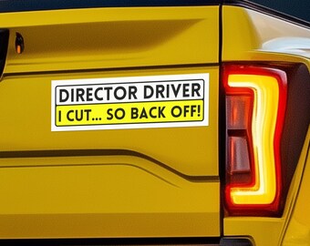 May include: A yellow truck with a white sticker that reads "Director Driver I cut... so back off!"