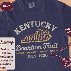 A navy t-shirt with "KENTUCKY BOURBON TRAIL" and a map of Kentucky printed in distressed cream and orange, with "Custom Text" and "Custom Date" tags.