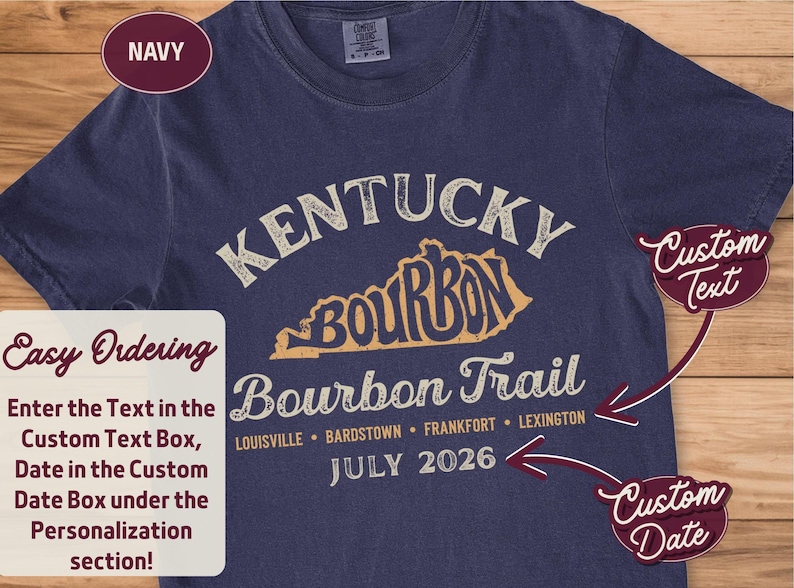 A navy blue t-shirt with "KENTUCKY BOURBON TRAIL" and a map of Kentucky printed in distressed cream-colored text, with "Louisville, Bardstown, Frankfort, Lexington" and "JULY 2026" below, with red arrows pointing to customizable text areas.
