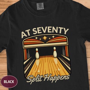 Può includere: T-shirt nero con grafica a tema bowling. Il design presenta una scena di bowling con birilli e la scritta "AT SEVENTY Split Happens" in stile retrò. La maglietta è di colore nero tinta unita.
