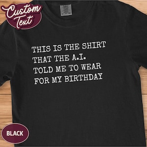 May include: Black t-shirt with white text: "THIS IS THE SHIRT THAT THE A.I. TOLD ME TO WEAR FOR MY BIRTHDAY." Includes a custom text label and a "BLACK" label. A casual tee, ideal for a birthday.
