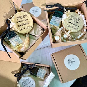 May include: Gift boxes with travel accessories. Each box contains a round pendant with Arabic text, a small perfume bottle, and a beaded bracelet or tassel. The boxes are brown with a white logo sticker. The items are presented as gifts.