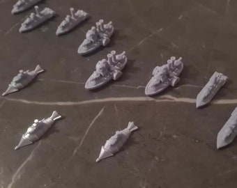 May include: A collection of 12 miniature grey plastic ships, including submarines and battleships, arranged on a grey surface.