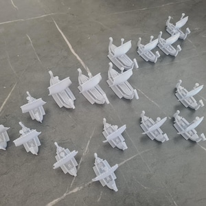 Puede incluir: Una colección de barcos en miniatura blancos, algunos con velas, dispuestos sobre una superficie gris.