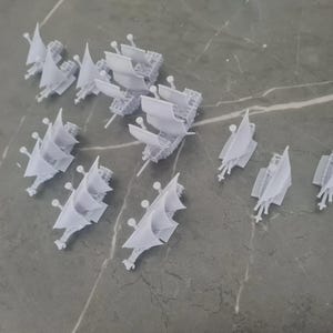 Puede incluir: Una colección de 10 barcos en miniatura blancos con velas. Los barcos están hechos de plástico y miden aproximadamente 5 cm de largo. Están dispuestos en un patrón aleatorio sobre una superficie gris.