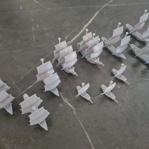 Puede incluir: Una colección de 15 barcos en miniatura blancos, algunos con velas, otros con mástiles, dispuestos sobre una superficie gris. Los barcos son de plástico y miden aproximadamente 5 cm de largo.