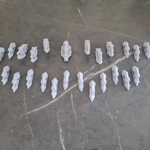 Puede incluir: Una colección de 25 barcos en miniatura blancos, algunos con velas, dispuestos en un patrón simétrico sobre una superficie gris.