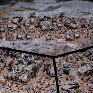 May include: A large collection of miniature wargaming figures and vehicles, painted in a weathered, post-apocalyptic style. The figures are arranged in battle formations on a grey, textured surface.