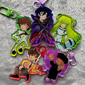 May include: Five acrylic keychains featuring anime-style characters. One shows a person in a white suit, another a figure in a dark purple cape, a third with long lime green hair, a fourth in a yellow blazer, and the fifth in a black school uniform.
