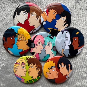 May include: A collection of seven circular pin-back buttons featuring colorful anime-style illustrations of pairs of characters facing each other. Each button displays distinct character designs with varied hair colors, facial features, and backgrounds.