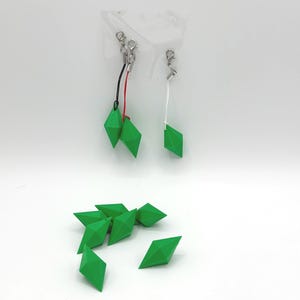 May include: A set of eight green diamond-shaped charms. Two of the charms are attached to silver keychains with black and white strings. The charms are made of plastic and have a glossy finish.