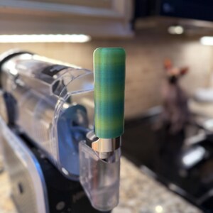 May include: A close-up of a green and blue 3D printed handle for a kitchen appliance.
