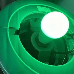 May include: A close-up of a green plastic object with a bright white light bulb. The text on the object reads, "Twist the bulb into the base to lock and secure in place."