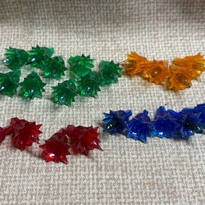 May include: A collection of vintage Christmas light covers in various colors. The assortment includes green, orange, red, and blue plastic covers, each with a starburst design. These decorative covers are designed to fit over light bulbs.