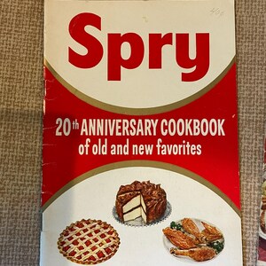 K&ouml;nnte beinhalten: Ein Vintage-Kochbuch mit dem Titel "Spry 20th Anniversary Cookbook of old and new favorites". Der Umschlag zeigt ein rotes und goldenes Design mit Illustrationen von einem Kuchen, einer Torte und Brath&auml;hnchen.