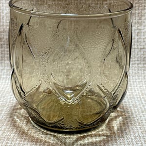 May include: A clear glass tumbler with a textured, diamond-shaped pattern. The glass has a brown tint.