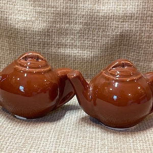 May include: A set of two brown ceramic teapot salt and pepper shakers. The shakers are small and have a rounded shape.