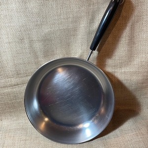 May include: A silver frying pan with a black handle. The pan has a shiny, metallic finish.