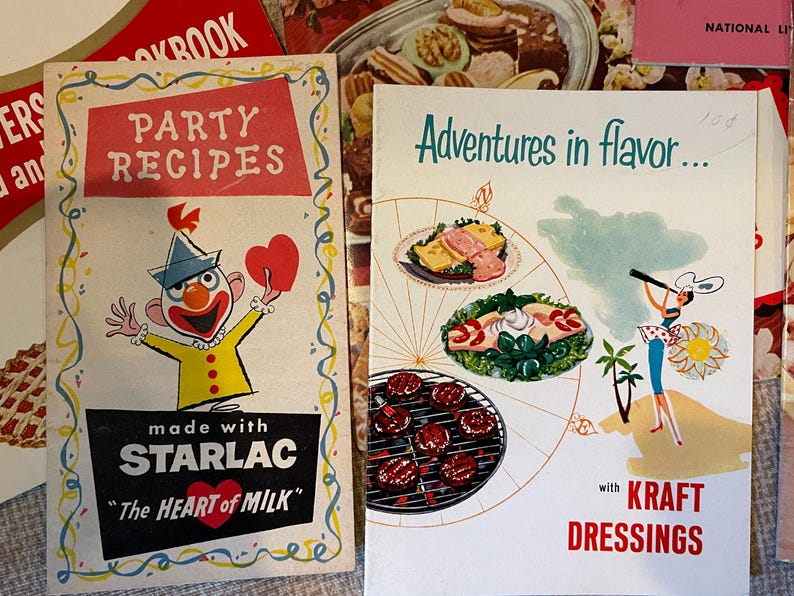 K&ouml;nnte beinhalten: Zwei Vintage-Kochb&uuml;cher mit bunten Umschl&auml;gen. Das erste Kochbuch zeigt einen Comic-Clown mit einem roten Herzen und dem Text "Party-Rezepte mit Starlac "Das Herz der Milch". Das zweite Kochbuch zeigt eine bunte Illustration eines Kompasses mit verschiedenen Lebensmitteln und dem Text "Abenteuer im Geschmack... mit Kraft Dressings".