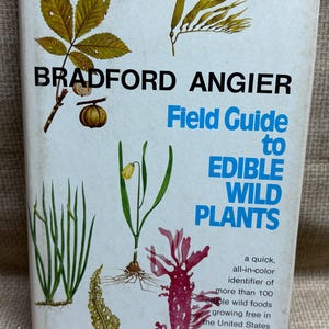 May include: A vintage field guide titled "Field Guide to Edible Wild Plants" by Bradford Angier. The cover features illustrations of various plants in green, yellow, and red, with text in black and blue. The book is a quick, all-in-color identifier of edible wild foods.