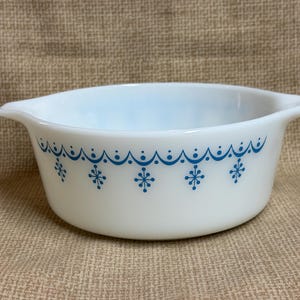May include: White Pyrex bowl with two handles and a blue snowflake and scalloped design. The bowl is round and has a light blue interior. A vintage kitchenware item.