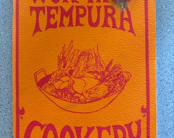 Puede incluir: Portada de libro de cocina naranja con el título "Wok and Tempura Cookery" en letras rojas. La portada presenta un dibujo de un wok lleno de comida.