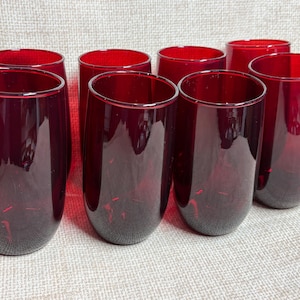 以下が含まれることがあります： 深紅色の脚のないグラス8個セット。グラスは滑らかで丸みを帯びた形状をしています。ニュートラルカラーの表面に配置されています。これらのグラスは、水、ジュース、またはその他の飲み物の提供に適しています。