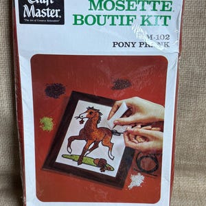 Op de afbeelding: Een Craft Master Mosette Boutif Kit, M-102, met een pony plank ontwerp. De kit bevat materialen om een 17,78 x 22,86 cm grote muurplaat van gemalen marmer te maken. De doos is rood en wit met de woorden "Craft Master".