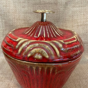 May include: Red ceramic bowl with a lid and a gold knob. The bowl has a textured design with white accents.