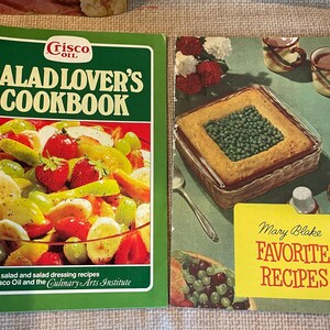 K&ouml;nnte beinhalten: Zwei Vintage-Kochb&uuml;cher, eines mit dem Titel "Salad Lover's Cookbook" mit einem Foto eines Obstsalats auf dem Cover und das andere mit dem Titel "Mary Blake Favorite Recipes" mit einem Foto einer Auflaufform gef&uuml;llt mit Erbsen auf dem Cover.