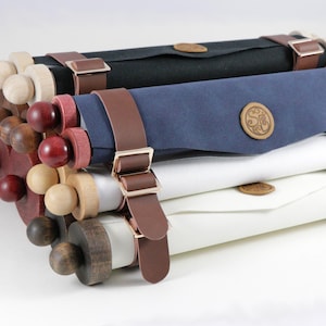 May include: A stack of four scroll cases in black, navy blue, white, and cream. Each case has a wooden roller with a decorative knob, leather straps, and a wooden emblem. The cases are stacked on top of each other.