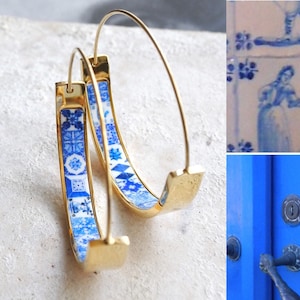 May include: A pair of gold hoop earrings with blue and white patterned tiles embedded in the metal. The tiles feature a geometric design.