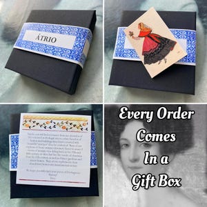 May include: A black gift box with a white label that says "&Aacute;TRIO" and a small image of a woman in a traditional Portuguese dress. The box is sitting on a white surface. The text "Every Order Comes In a Gift Box" is written in white on a black background.