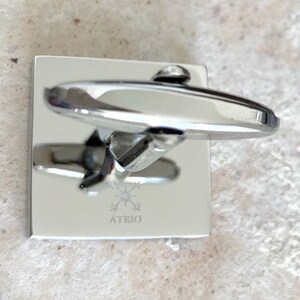 May include: Silver cufflinks with a square base and a rounded top. The cufflinks have a logo engraved on the base that says "ATRIO" with a starburst design.