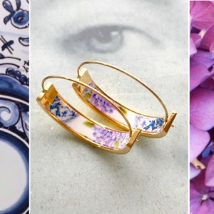May include: A pair of gold hoop earrings with a white background and a purple floral design.