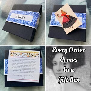 May include: A black gift box with a white label that says "&Aacute;TRIO" and a small image of a woman in a traditional Portuguese dress. The box is sitting on a white surface. The text "Every Order Comes In a Gift Box" is written in white letters on a black background.